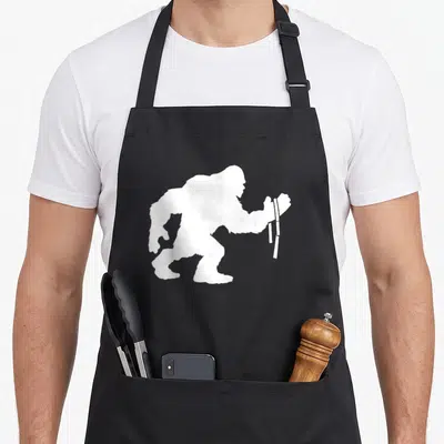 Tablier de cuisine noir avec silhouette blanche d'un Bigfoot Wrestler tenant une barre de lutte bras