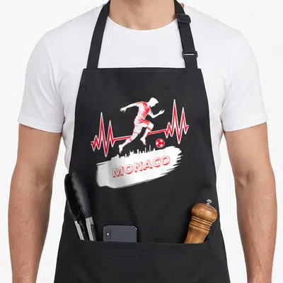 Tablier de cuisine noir avec silhouette de footballeur rouge et inscription MONACO sur fond blanc.