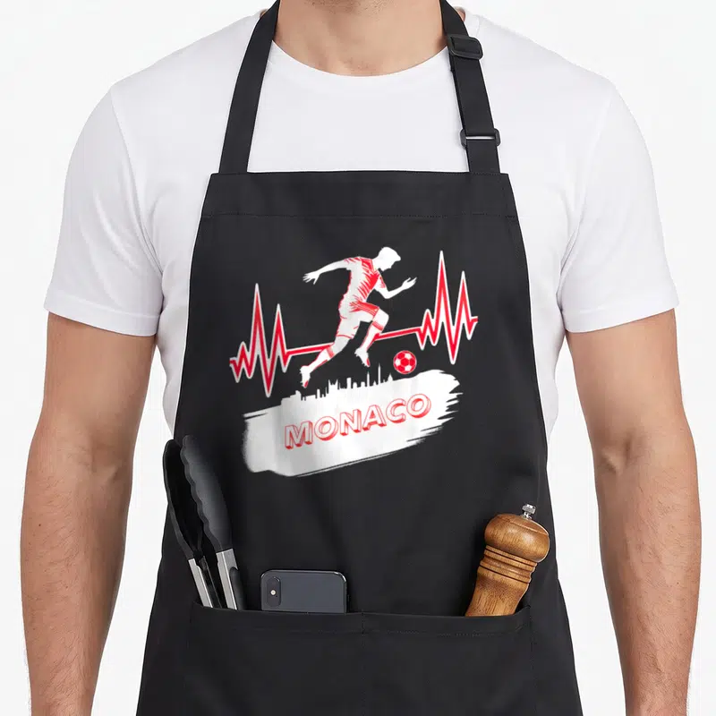 Tablier de cuisine noir avec silhouette de footballeur rouge et inscription MONACO sur fond blanc.