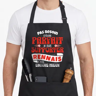 Tablier de cuisine noir avec le texte Pas Besoin d'être Parfait je suis Supporter Rennais c'est Encore Mieux en rouge et blanc.