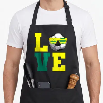 Tablier de cuisine noir avec le mot Love et un ballon de foot portant des lunettes vertes et jaunes ornées d'étoiles dorées.