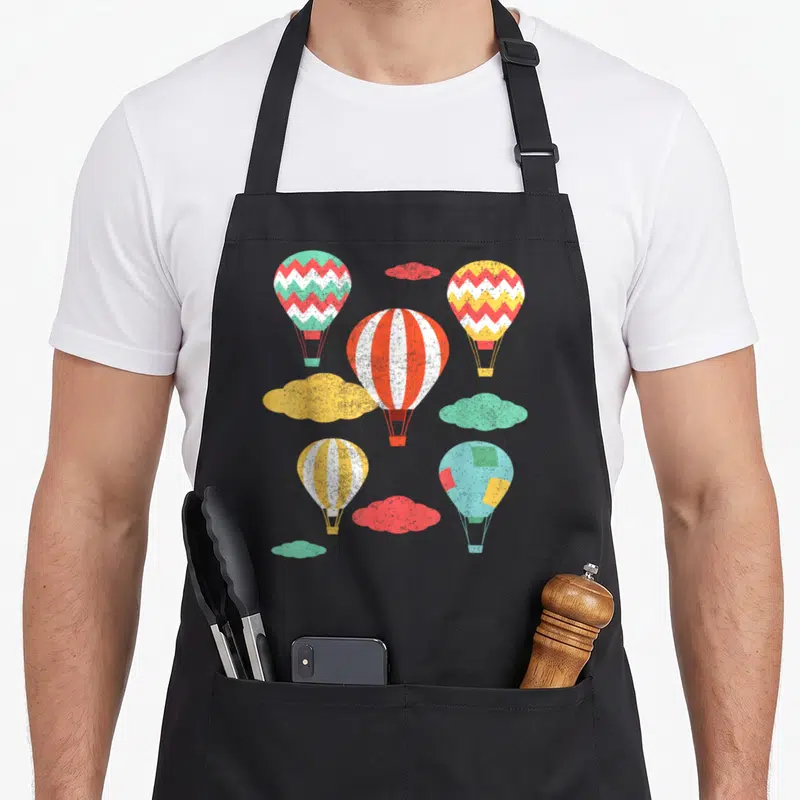 Tablier de cuisine noir avec cinq montgolfières colorées et nuages stylisés dans un design vintage.