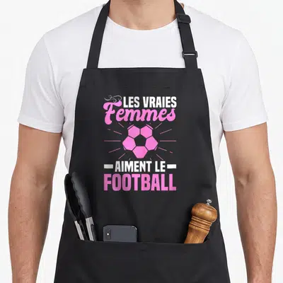 Tablier de cuisine noir avec inscription Les Vraies Femmes Aiment Le Football et ballon rose stylisé.