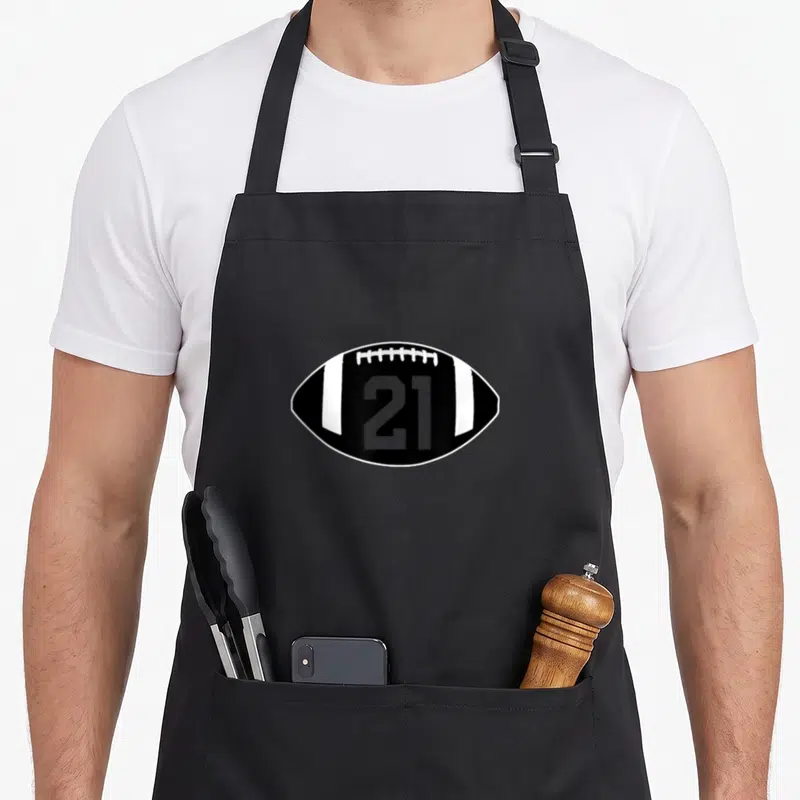 Tablier de cuisine noir avec un motif de ballon de rugby noir portant le numéro 21 en gris.