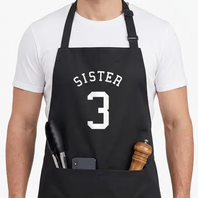 Tablier de cuisine noir avec inscription blanche Sister au-dessus du grand chiffre 3 style maillot.
