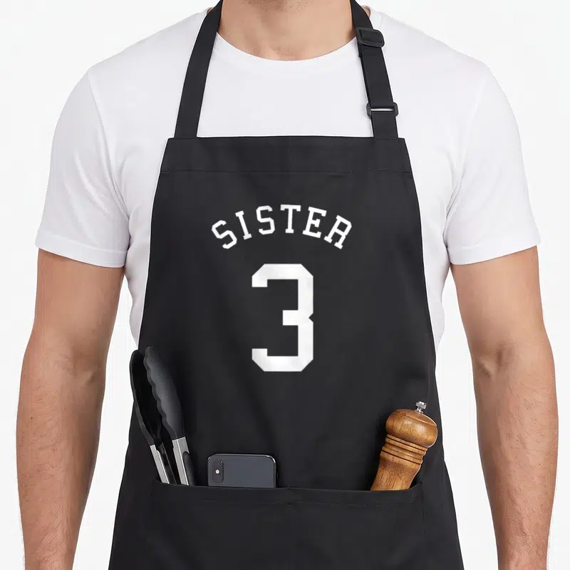 Tablier de cuisine noir avec inscription blanche Sister au-dessus du grand chiffre 3 style maillot.