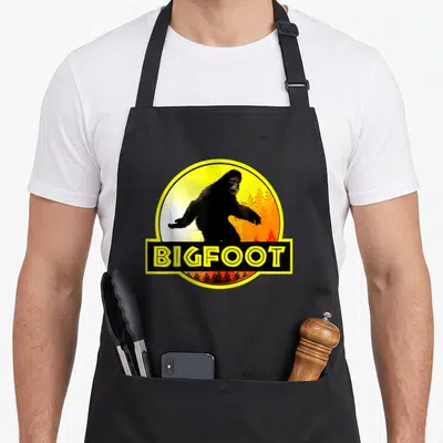 Tablier de cuisine noir avec illustration circulaire de Bigfoot et texteBIGFOOT en jaune vif.