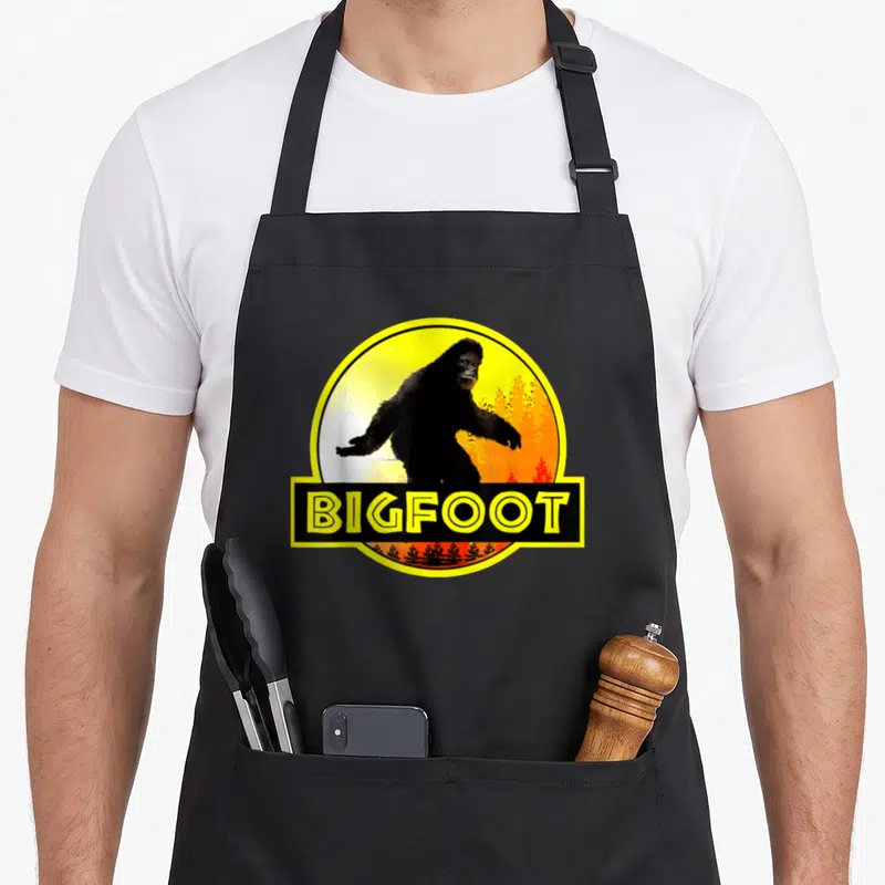 Tablier de cuisine noir avec illustration circulaire de Bigfoot et texteBIGFOOT en jaune vif.