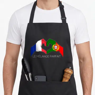 Tablier de cuisine noir avec deux mains formant un cœur aux drapeaux français et portugais et le texte le mélange parfait.