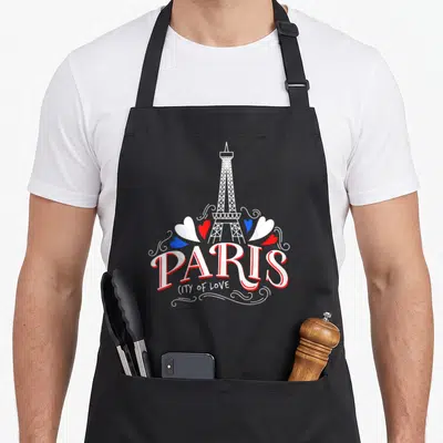 Tablier de cuisine noir avec une illustration de la tour Eiffel, des cœurs tricolores et le mot PARIS en lettres capitales blanches et rouges.