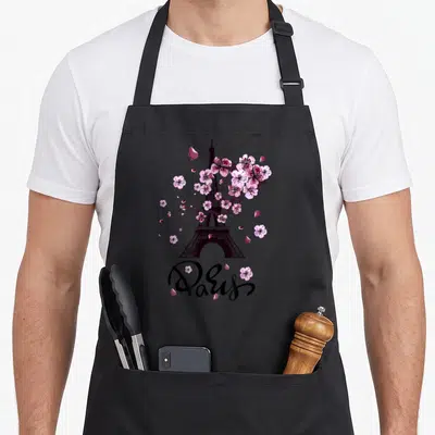 Tablier de cuisine noir avec une tour Eiffel entourée de fleurs roses et l'inscription Paris en calligraphie.