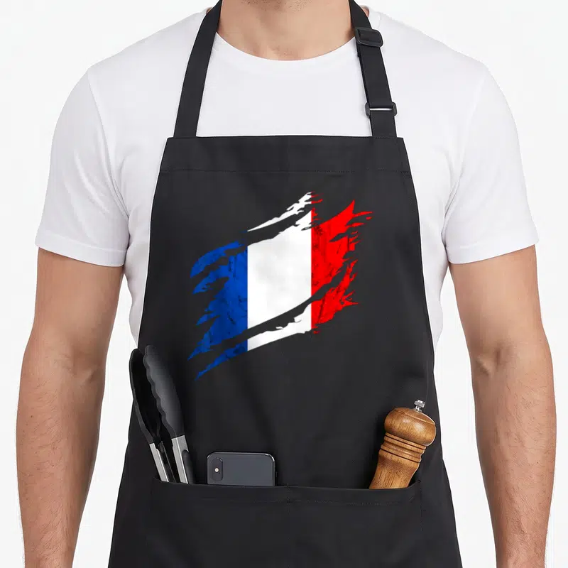 Tablier de cuisine noir avec un drapeau français stylisé aux bords effilochés et textures vieillies.