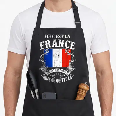 Tablier de cuisine noir avec inscription Ici C'est La France et drapeau tricolore orné de motifs floraux blancs.