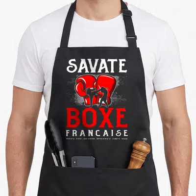 Tablier de cuisine noir avec inscription Savate Boxe Française et illustration de gants rouges surplombant des silhouettes en combat.