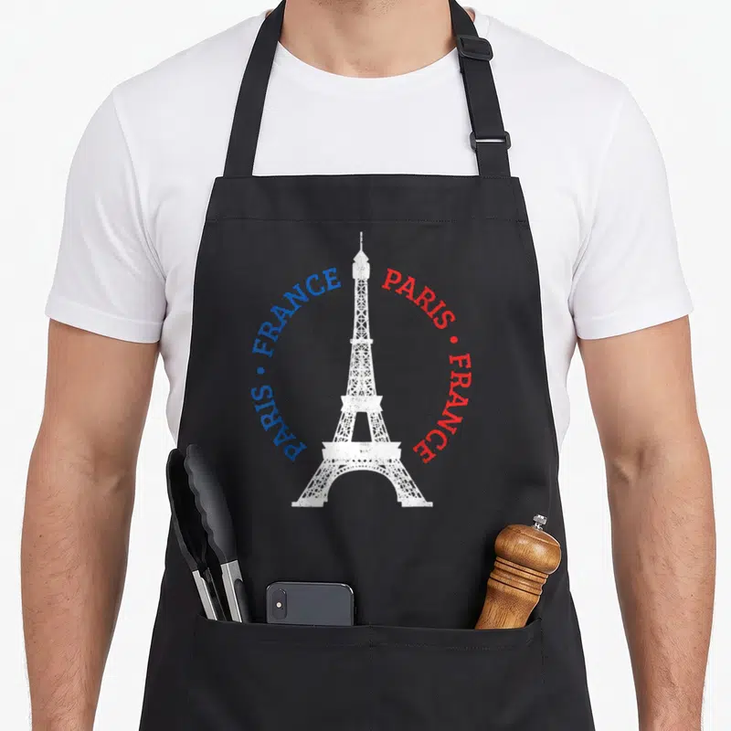 Tablier de cuisine noir avec une Tour Eiffel blanche et les mots PARIS FRANCE en bleu et rouge.