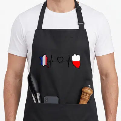 Tablier de cuisine noir avec une carte de France et une silhouette polonaise reliées par un cœur et un rythme cardiaque.