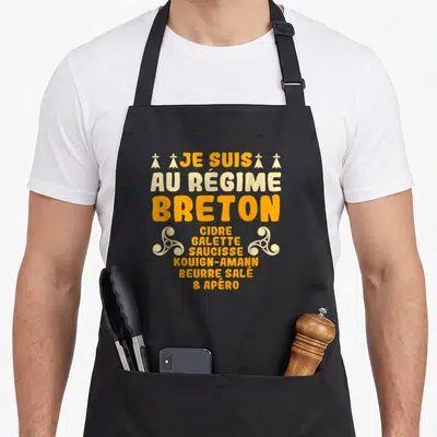 Tablier de cuisine noir avec inscription Je suis au régime breton et liste de spécialités en orange et crème.