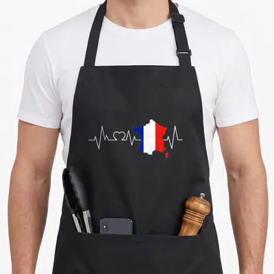 Tablier de cuisine noir avec une carte de France tricolore traversée par une ligne blanche en forme de rythme cardiaque et de cœur.