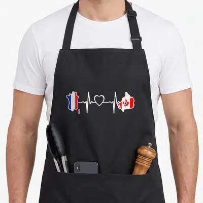 Tablier de cuisine noir avec carte de France et Canada reliées par un tracé de rythme cardiaque blanc et un cœur.
