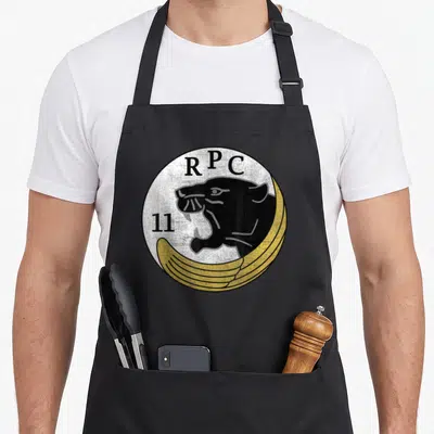 Tablier de cuisine noir avec logo circulaire RPC 11, tête de panthère noire et ailes dorées sur fond blanc texturé.