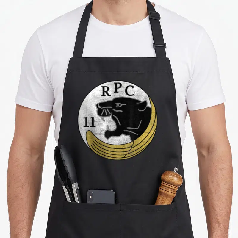 Tablier de cuisine noir avec logo circulaire RPC 11, tête de panthère noire et ailes dorées sur fond blanc texturé.