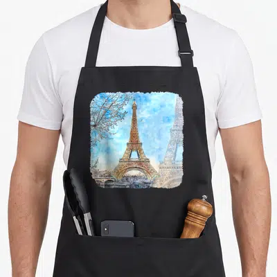 Tablier de cuisine noir avec une illustration aquarellée de la Tour Eiffel sur fond de ciel bleu nuageux.