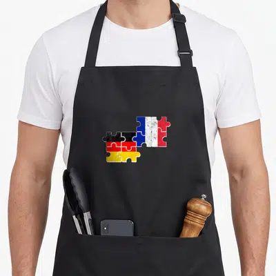 Tablier de cuisine noir avec drapeaux français et allemand en puzzle vintage superposés au centre.