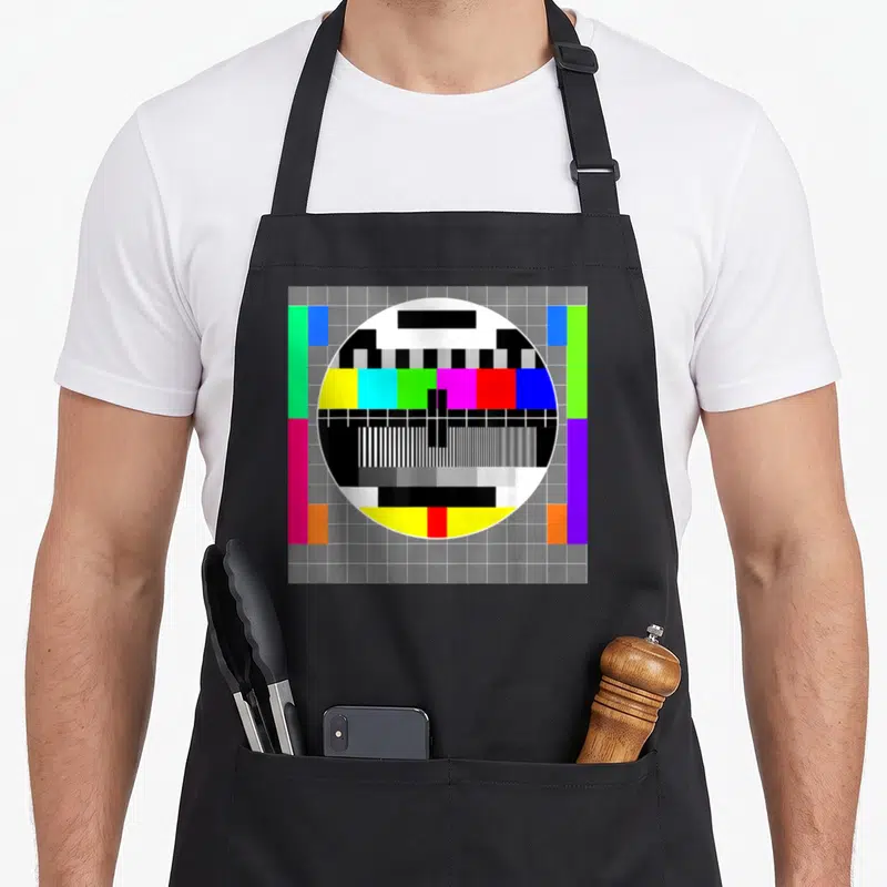 Tablier de cuisine noir avec un test pattern télévision rétro aux bandes colorées et grille grise.