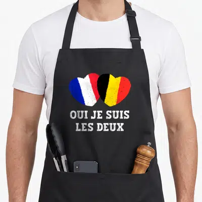 Tablier de cuisine noir avec un cœur formé des drapeaux français et belge et le texte Oui je suis les deux en blanc.