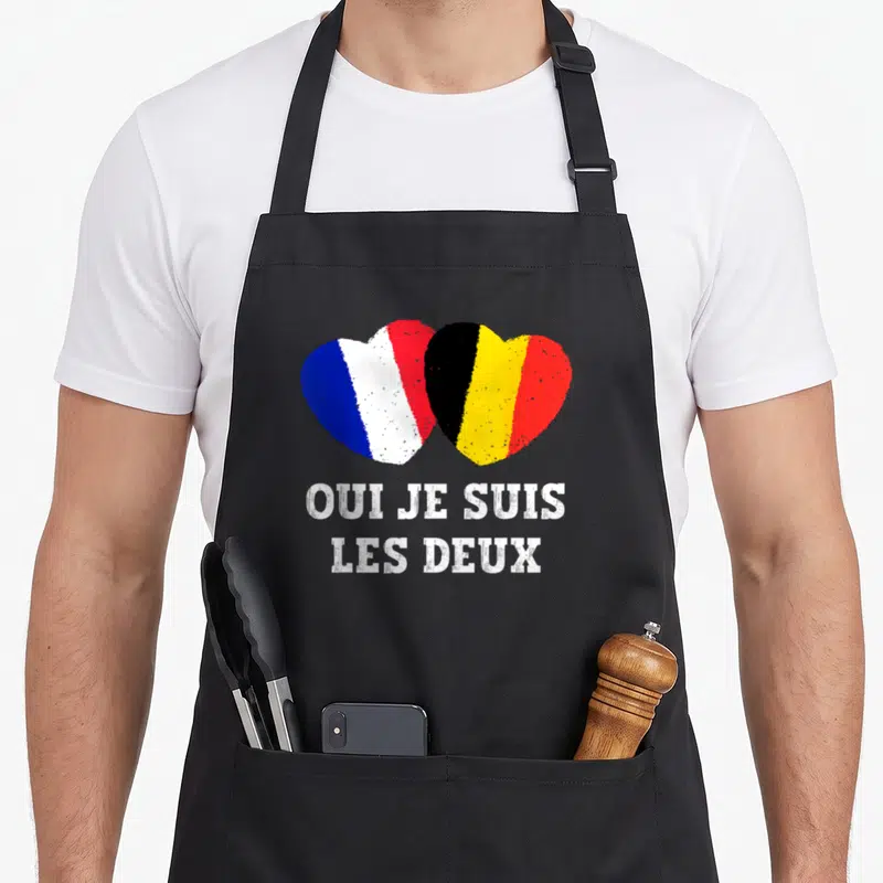 Tablier de cuisine noir avec un cœur formé des drapeaux français et belge et le texte Oui je suis les deux en blanc.
