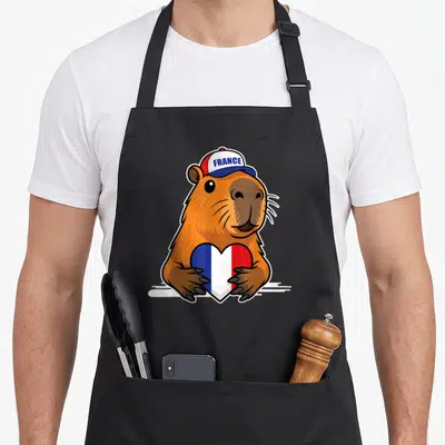 Tablier de cuisine noir avec illustration d'un capybara tenant un cœur tricolore français et coiffé d'une casquette.