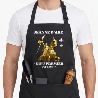 Tablier de cuisine noir avec statue dorée de Jeanne d'Arc et inscription Dieu premier servi en blanc.