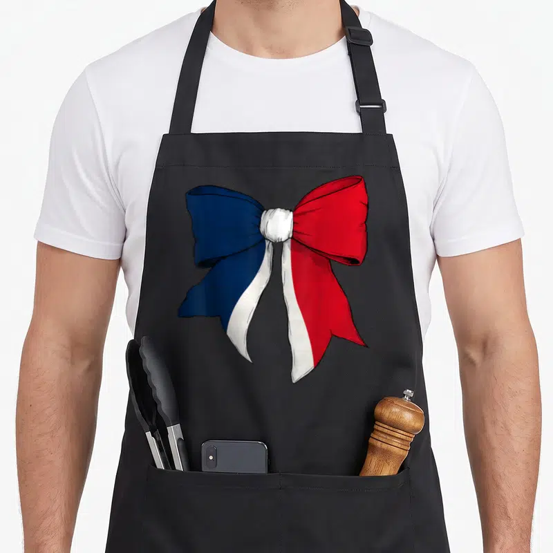 Tablier de cuisine noir avec un grand ruban coquette aux couleurs bleu blanc rouge du drapeau français imprimé au centre.