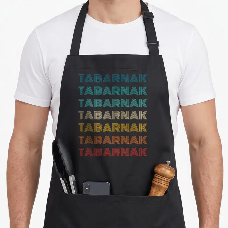 Tablier de cuisine noir avec le mot Tabarnak répété sept fois en lettres rayées multicolores.