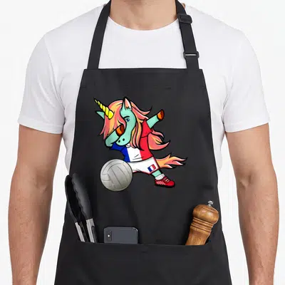 Tablier de cuisine noir avec une licorne aux cheveux roses effectuant un dab au-dessus d'un ballon de volley-ball tricolore.