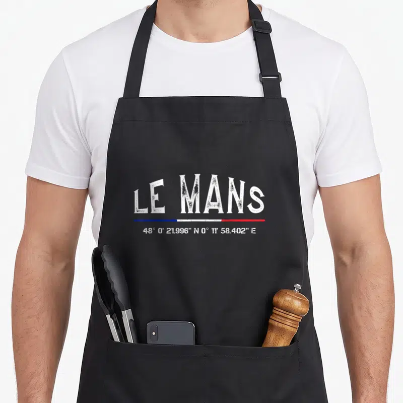 Tablier de cuisine noir avec inscription Le Mans, drapeau tricolore et coordonnées géographiques en blanc.