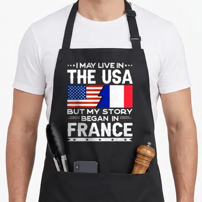 Tablier de cuisine noir avec les drapeaux américain et français et du texte blanc sur fond uni.