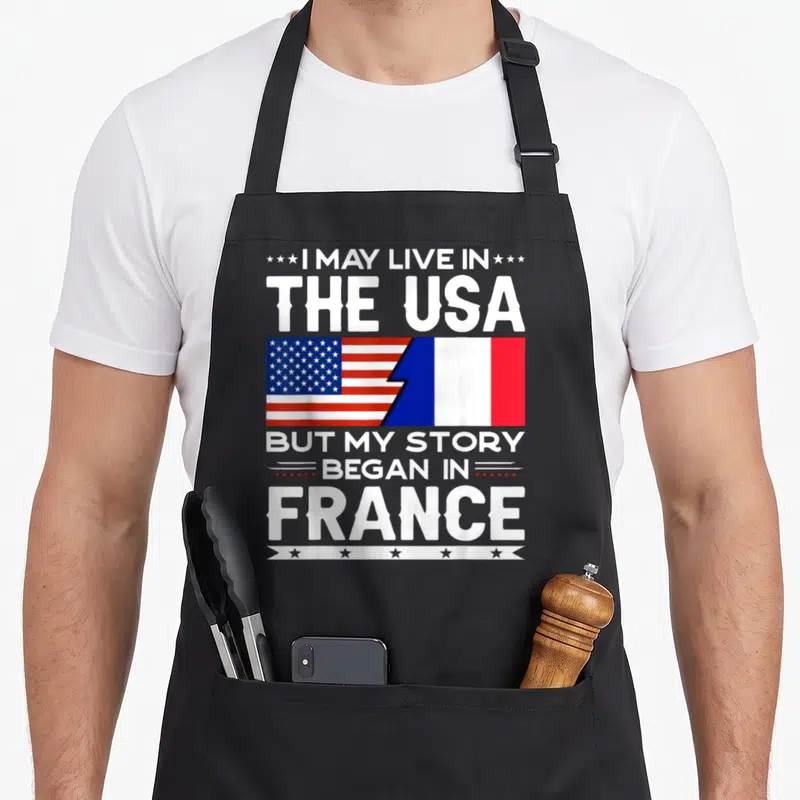 Tablier de cuisine noir avec les drapeaux américain et français et du texte blanc sur fond uni.
