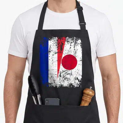 Tablier de cuisine noir avec un drapeau français et un cercle rouge japonais superposés sur fond blanc texturé.