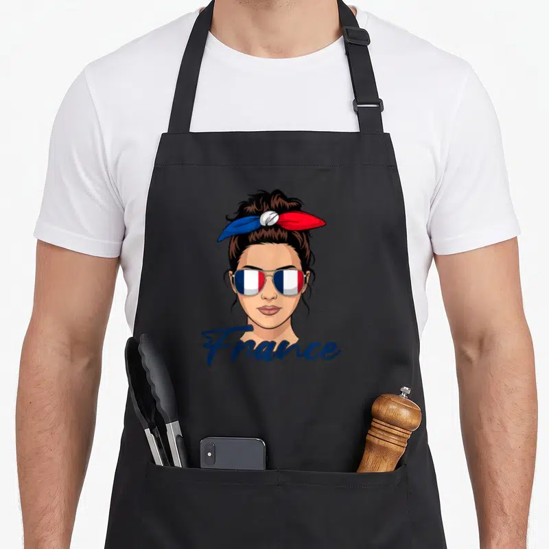 Tablier de cuisine noir avec une fille aux lunettes au drapeau français et un foulard tricolore dans les cheveux.