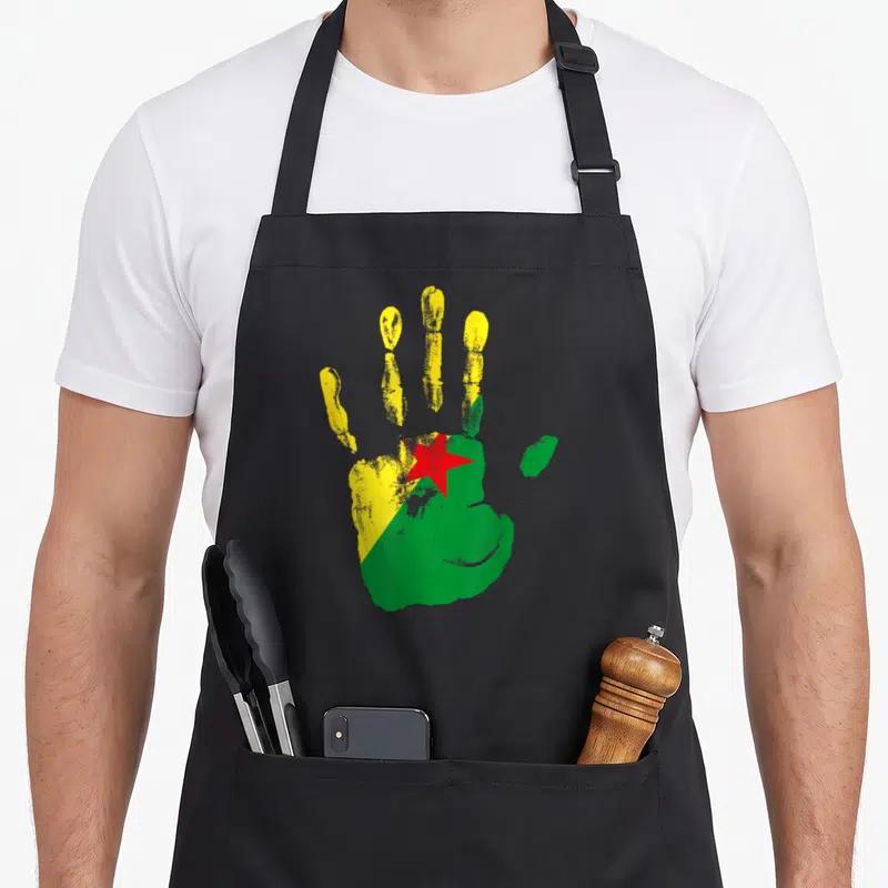 Tablier de cuisine noir avec une main peinte aux couleurs du drapeau de la Guyane Française, jaune et vert avec une étoile rouge.