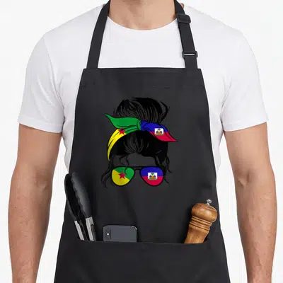 Tablier de cuisine noir avec illustration d'un profil féminin au bandana et lunettes aux couleurs des drapeaux guyanais et haïtiens.