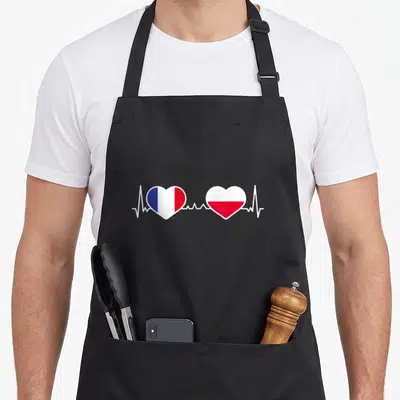 Tablier de cuisine noir avec deux cœurs aux drapeaux français et polonais reliés par une ligne de cœur blanche.