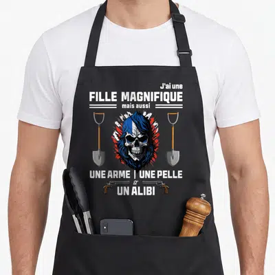 Tablier de cuisine noir avec un crâne aux cheveux bleus, deux pelles et des revolvers imprimés en blanc.