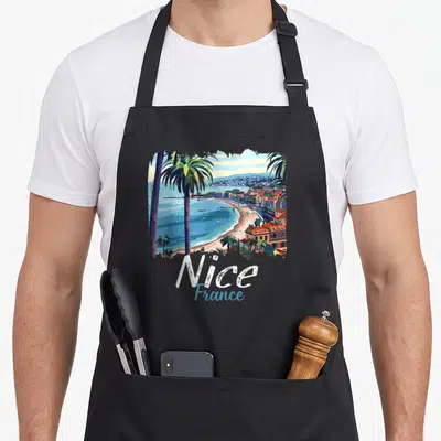 Tablier de cuisine noir avec illustration colorée de Nice, palmiers, plage et texte Nice France en bas du motif.