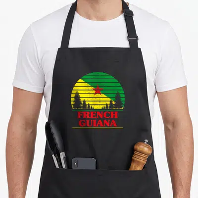 Tablier de cuisine noir avec un motif circulaire aux couleurs vert et jaune et l'inscription French Guiana en rouge.