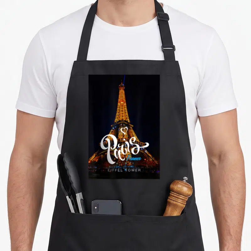 Tablier de cuisine noir avec la Tour Eiffel illuminée et le mot Paris en calligraphie blanche sur fond nocturne.