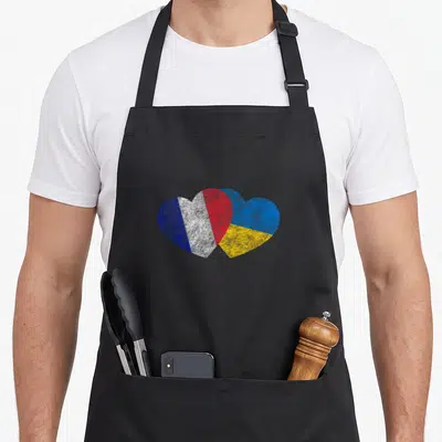 Tablier de cuisine noir avec deux cœurs superposés aux couleurs des drapeaux français et ukrainien en texture usée.
