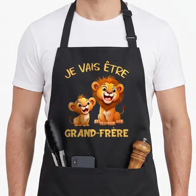 Tablier de cuisine noir avec deux lions colorés et le texte Je vais être grand-frère imprimé en jaune.