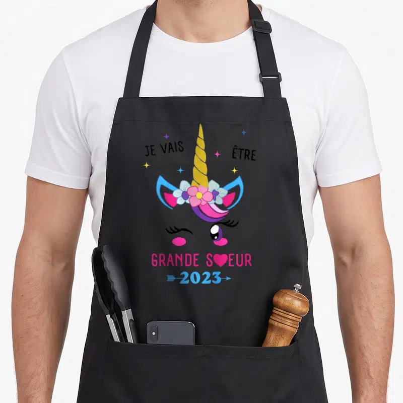 Tablier de cuisine noir avec illustration de licorne rose et texte Je vais être grande sœur 2023.